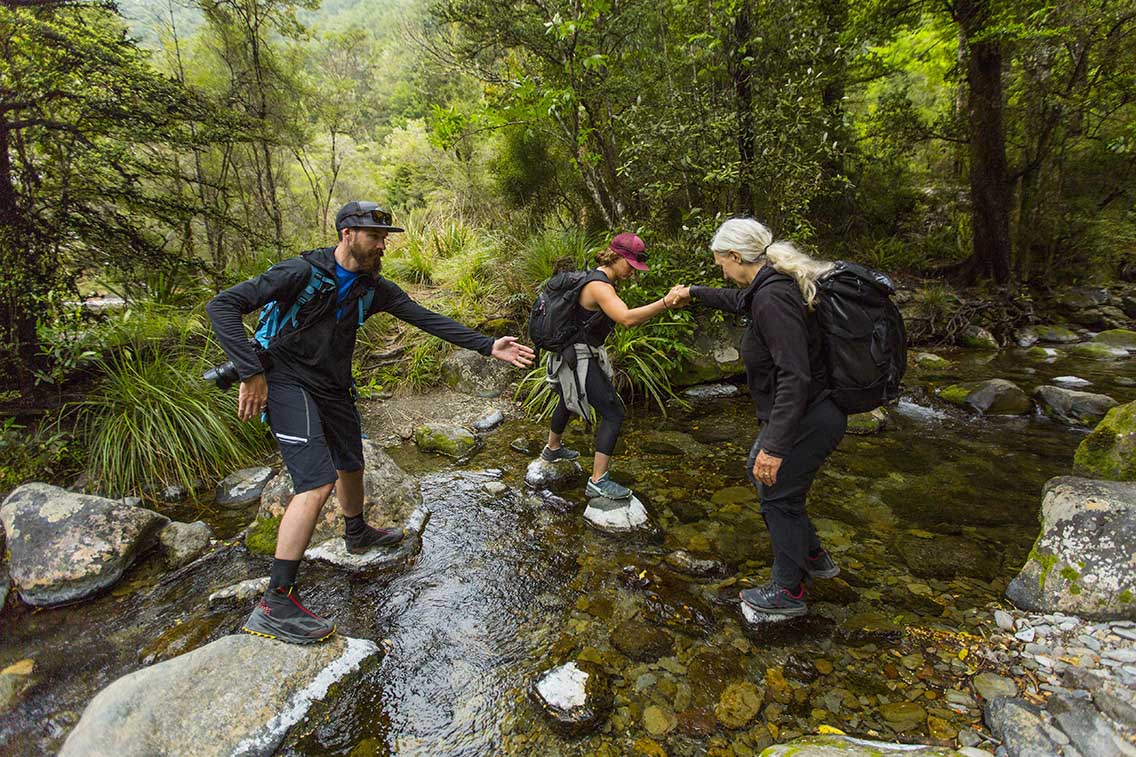 three people walking over a brook