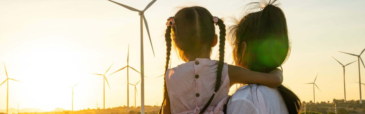 A woman and a girl looking at a windmill park in the sunset