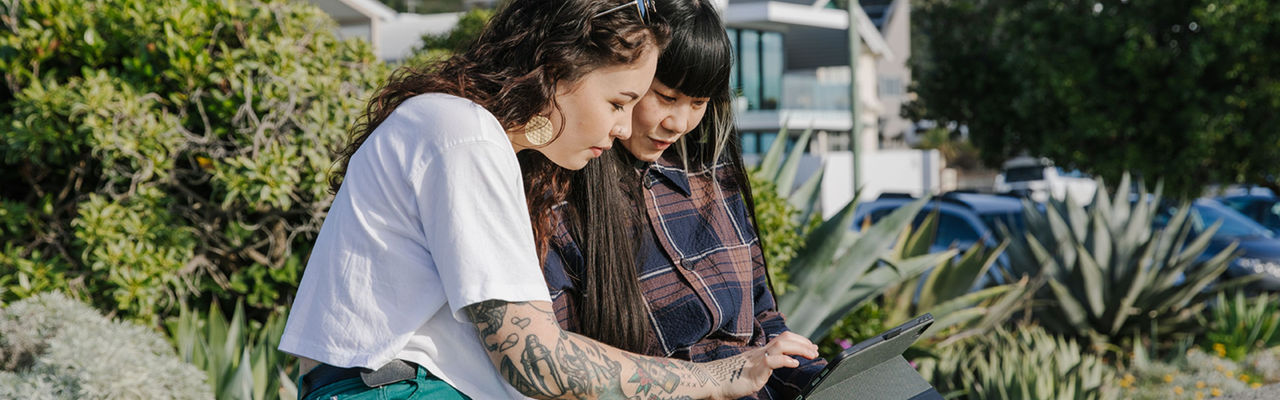 Two girls sitting outside looking at a tablet and smiling