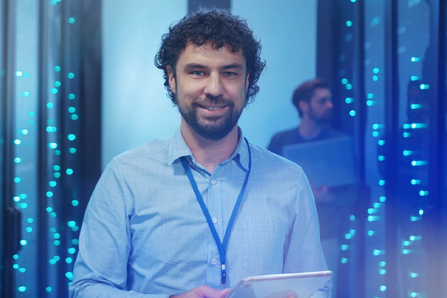 Two people in a server room with a tablet and laptop, surrounded by blue-lit server racks.