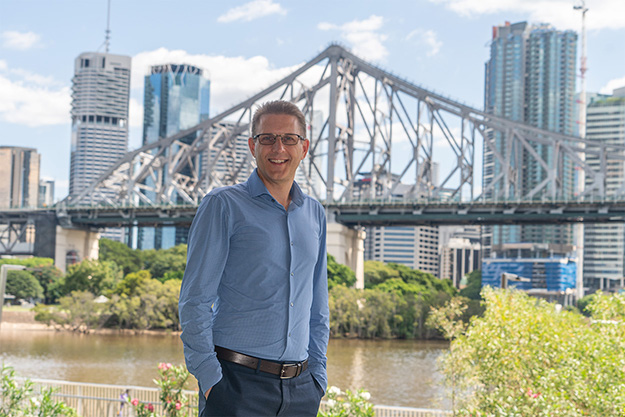 Mark Tile standing in front of bridge and a cityscape backdrop