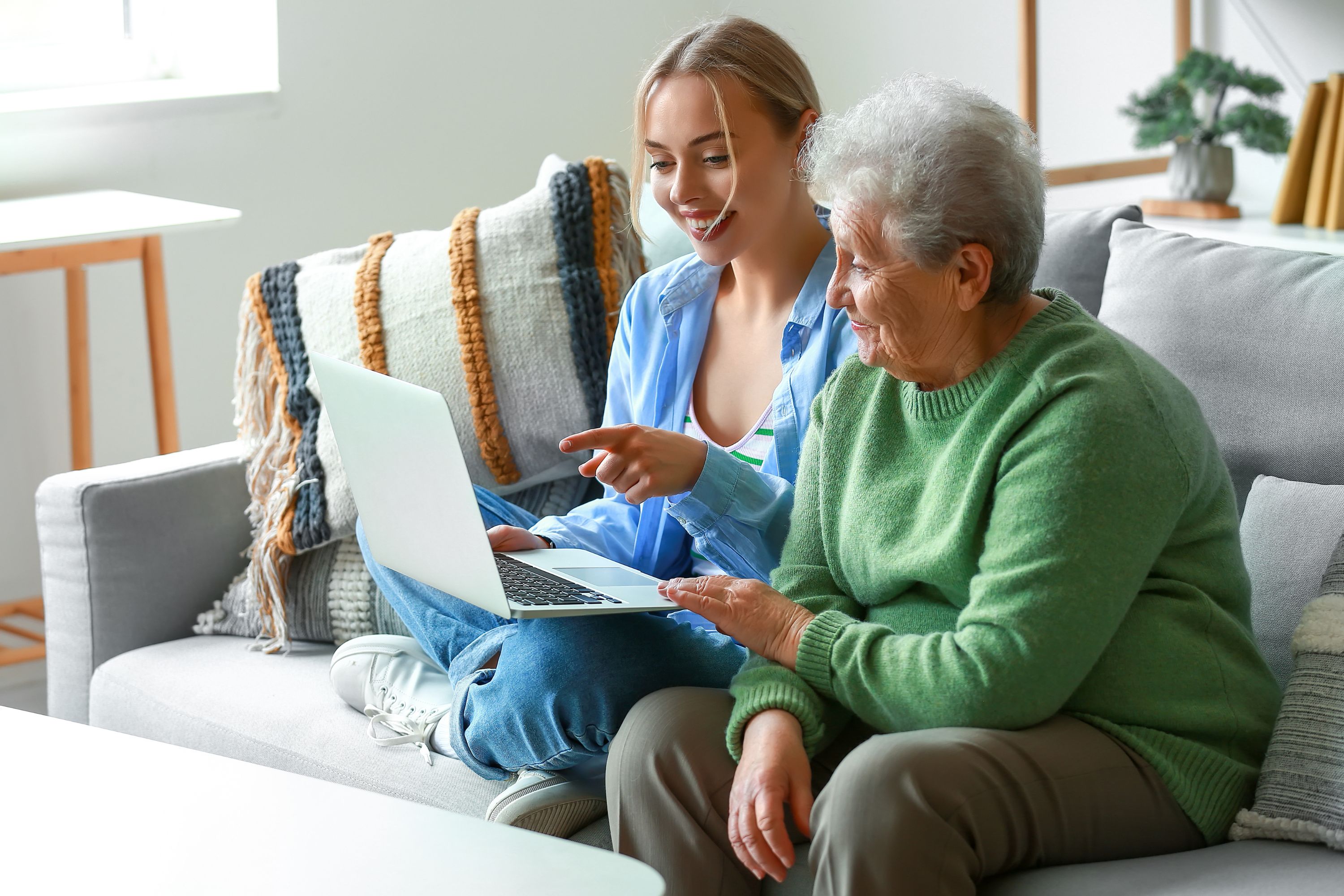 Photo of younger woman sitting with an elderly woman, pointing to something on a laptop screen