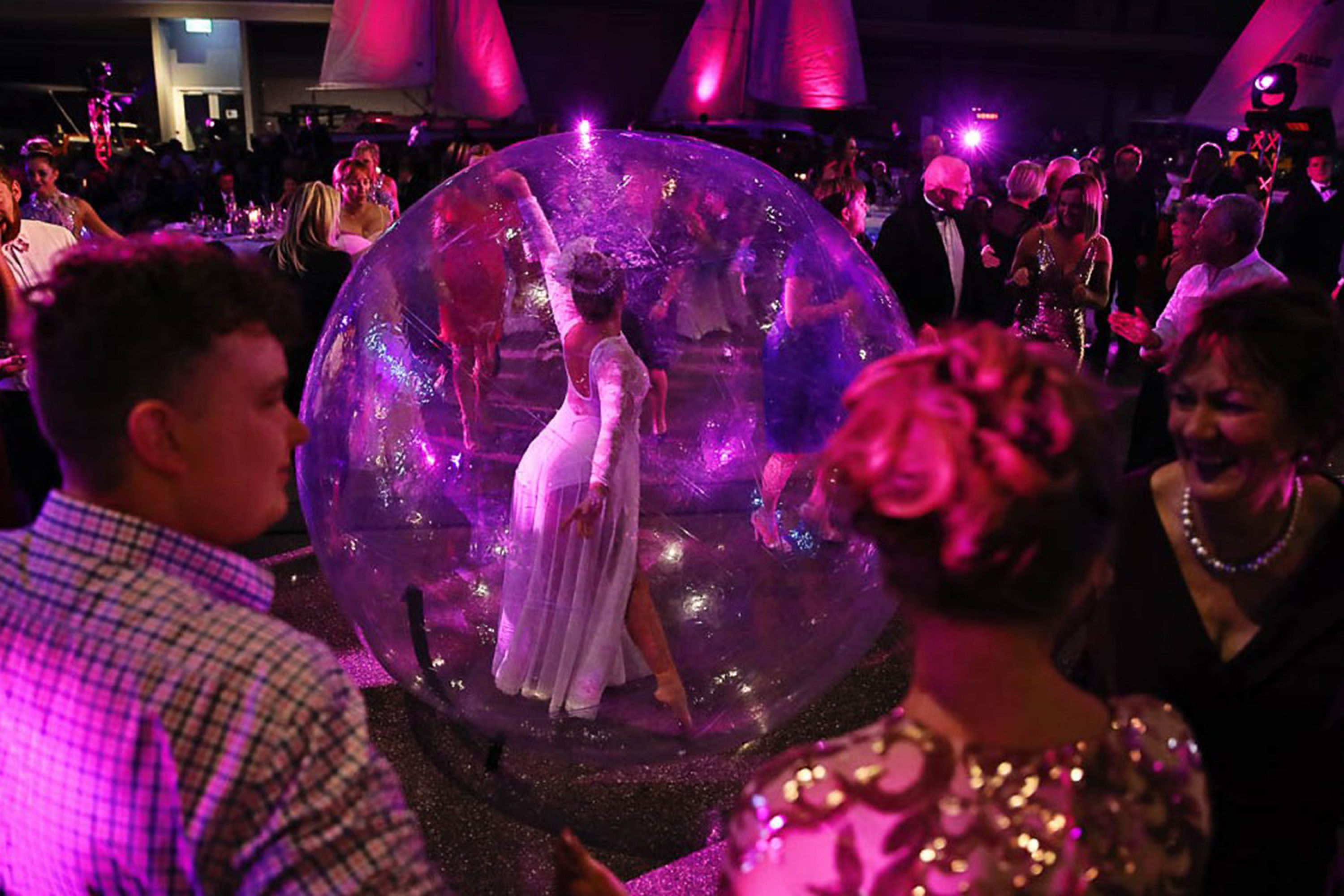 A dance floor with a dancer inside a bubble surrounded by people 