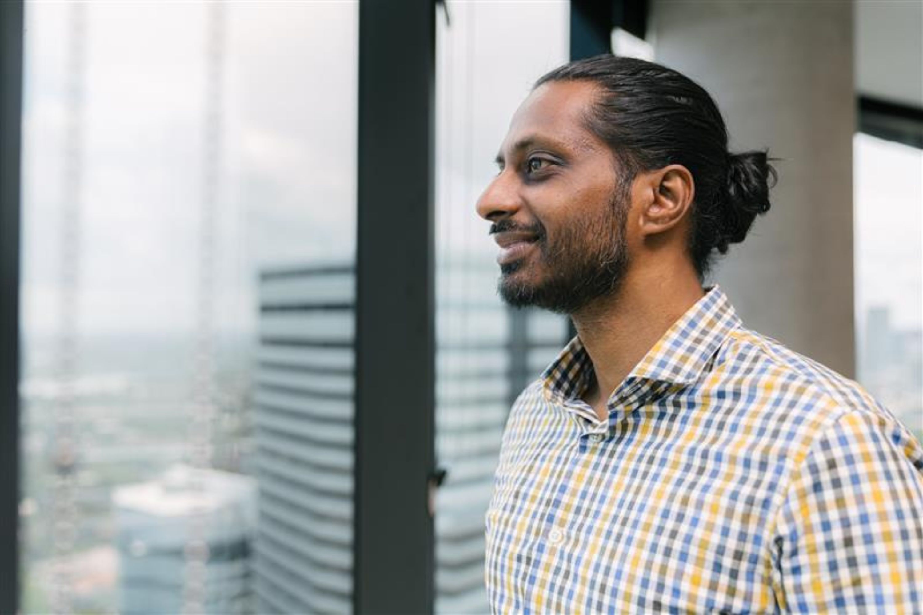 Side profile photograph of Vickesh looking out of a window over a city view.