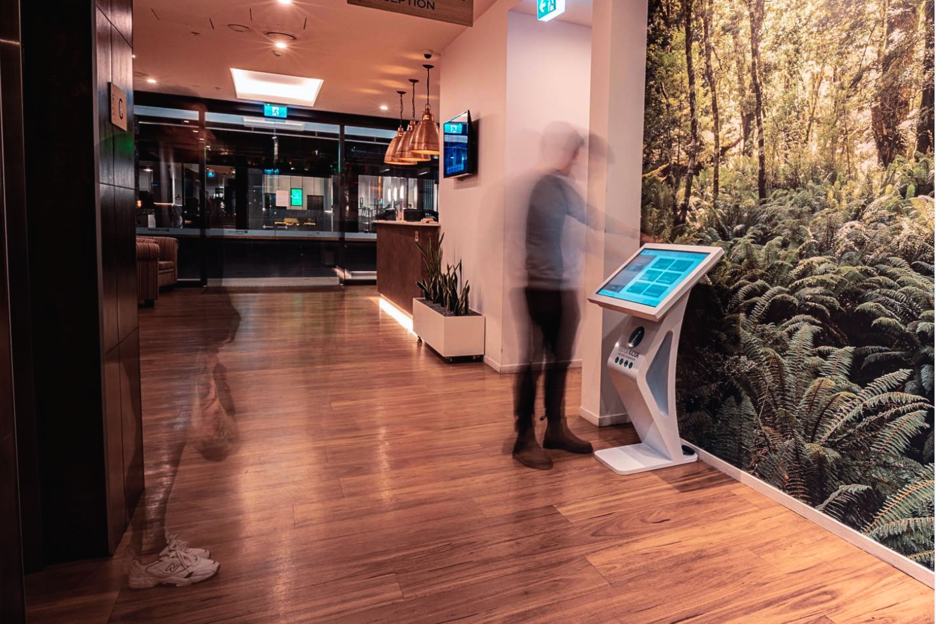 Long exposure photo of a man using a visitor kiosk booth in the warmly lit lobby of a hotel