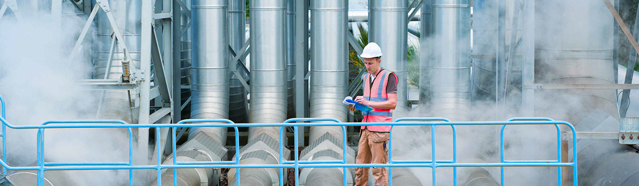 A worker standing on a walkway in front of large power station pipes