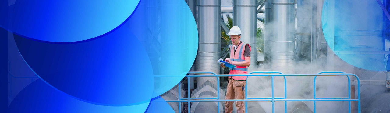 A worker standing on a walkway in front of large power station pipes