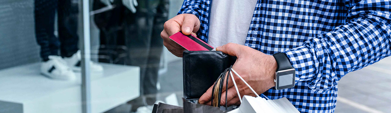 A man sliding a credit card into his wallet while holding shopping bags