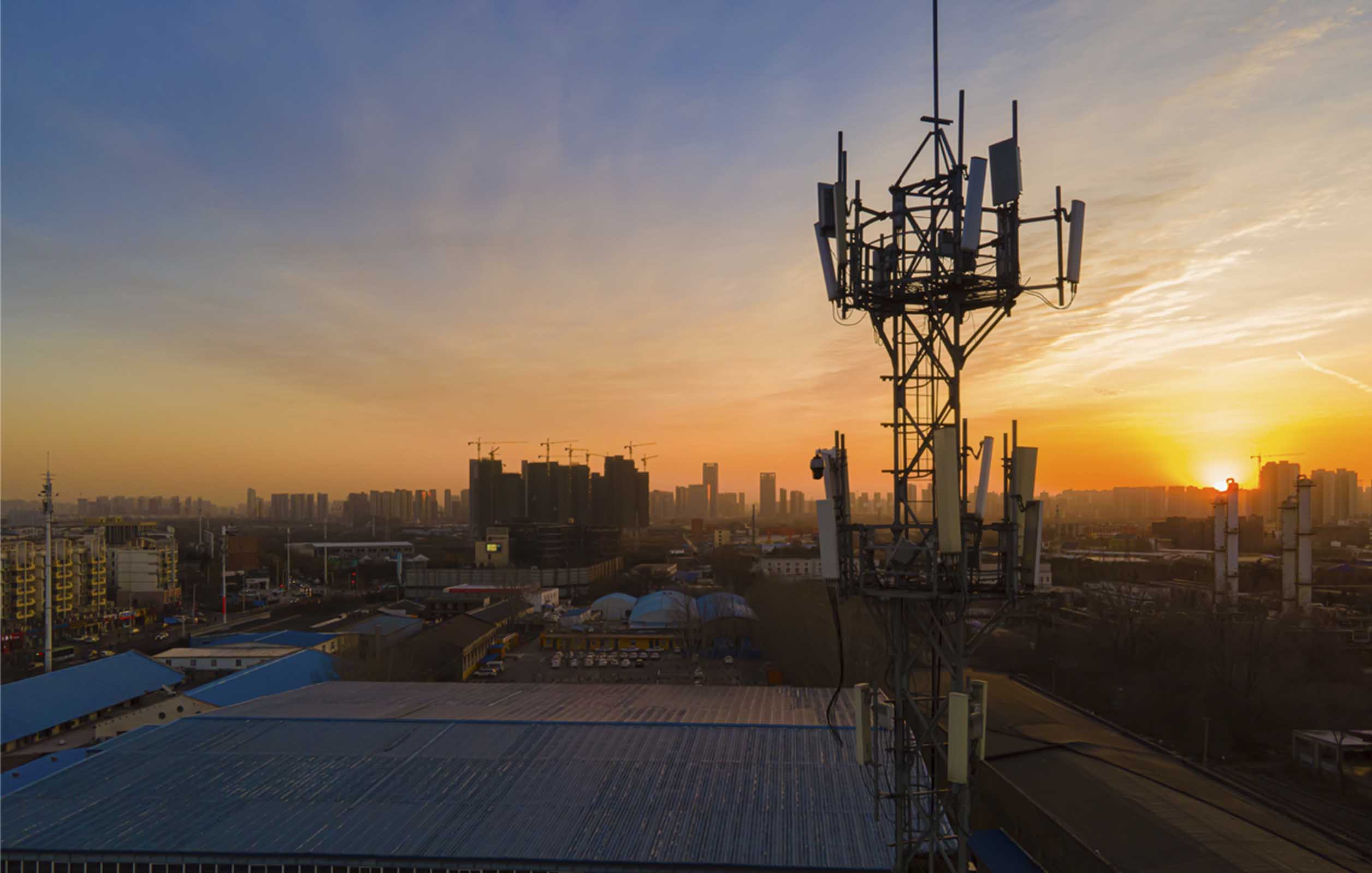 A wide shot of a cell tower against a cityscape sunset