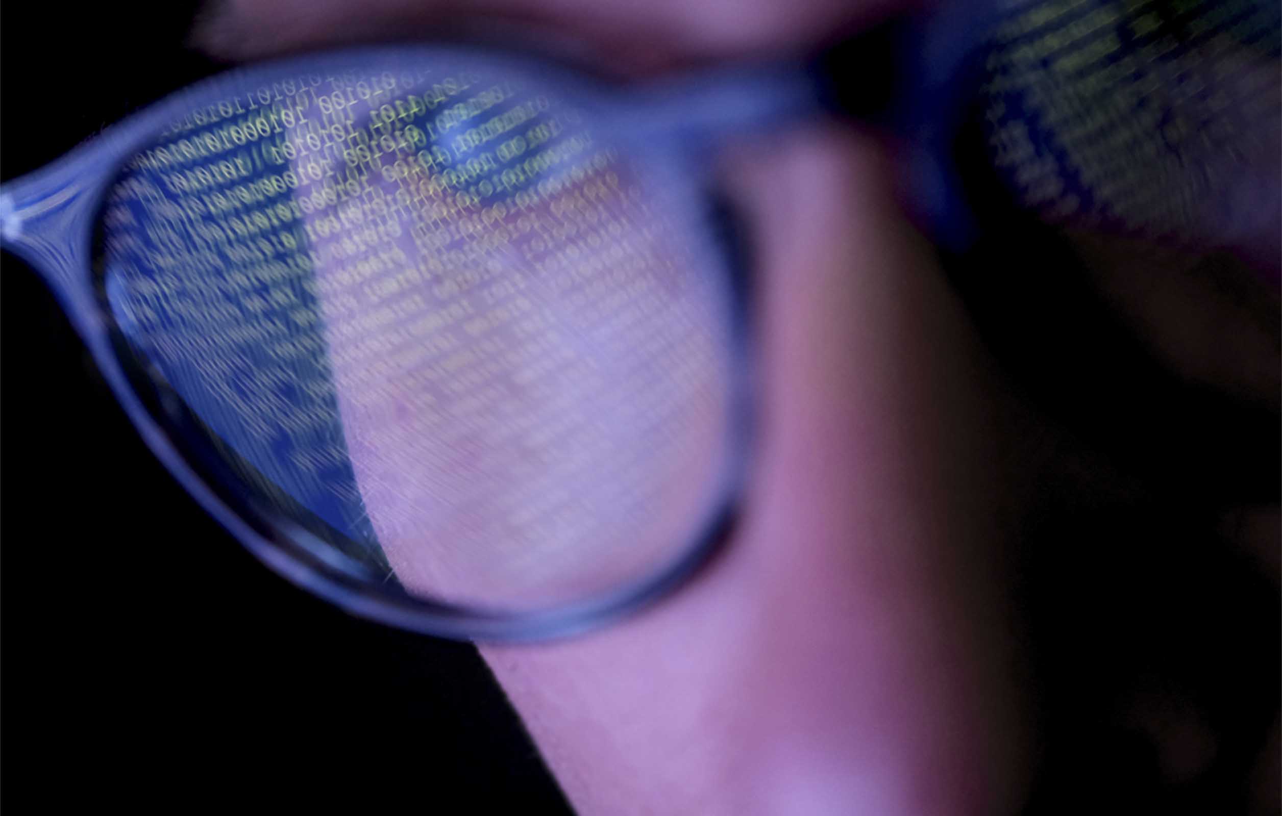 A close up shot of a person wearing glasses with code reflecting in the lenses