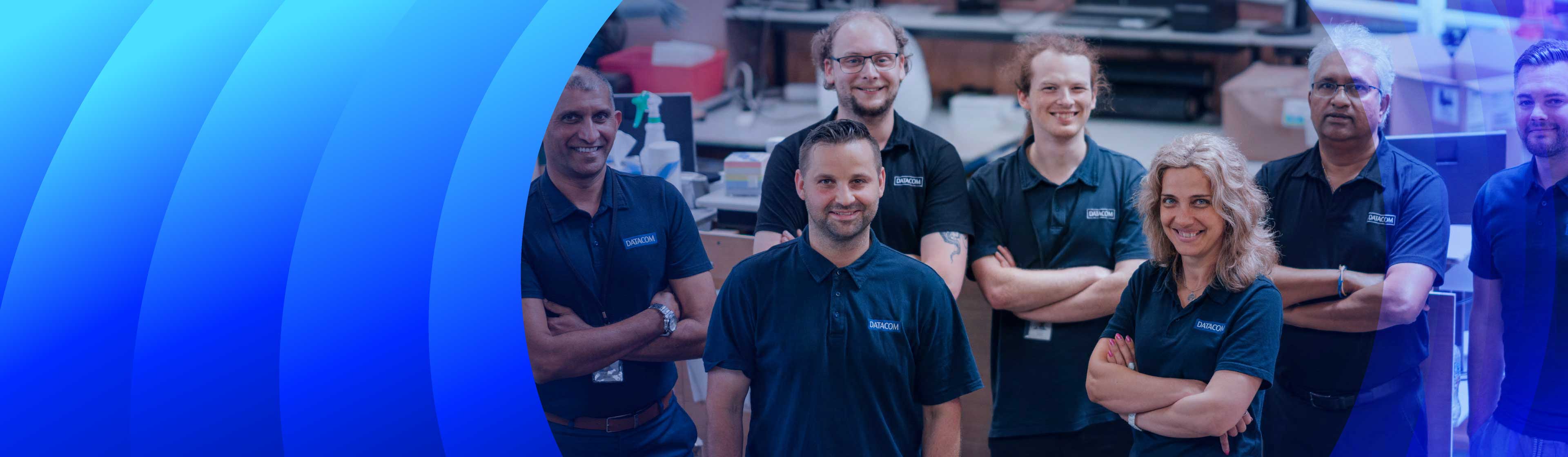 A group of Datacom employees wearing navy blue Datacom branded polo shirts smiling at the camera