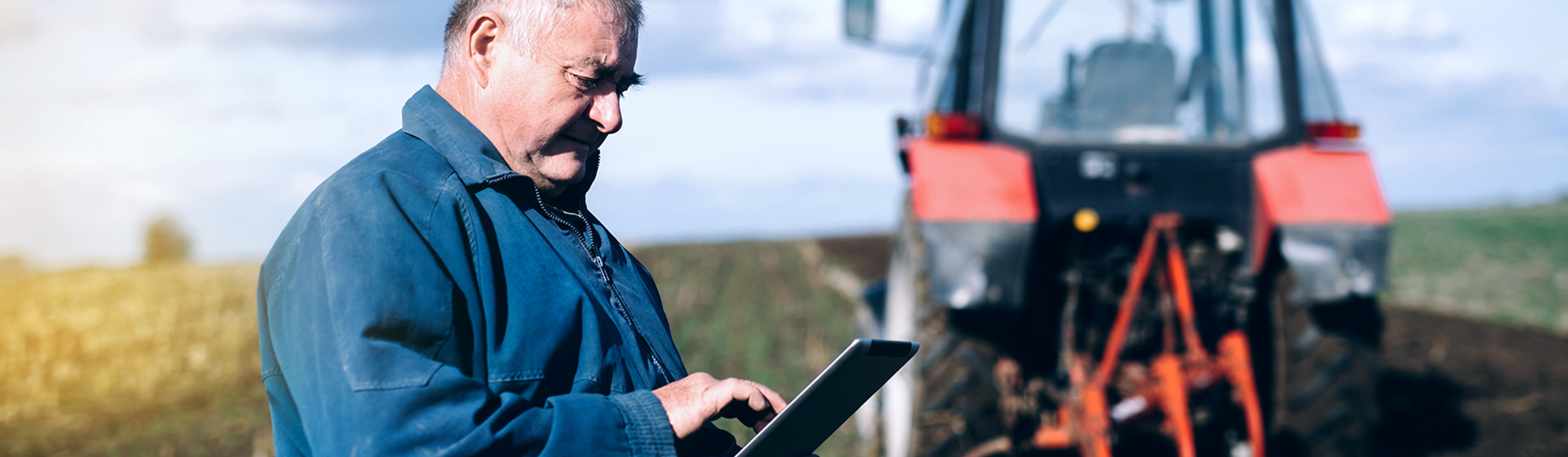 Framer using a tablet on field with red tractor in the background