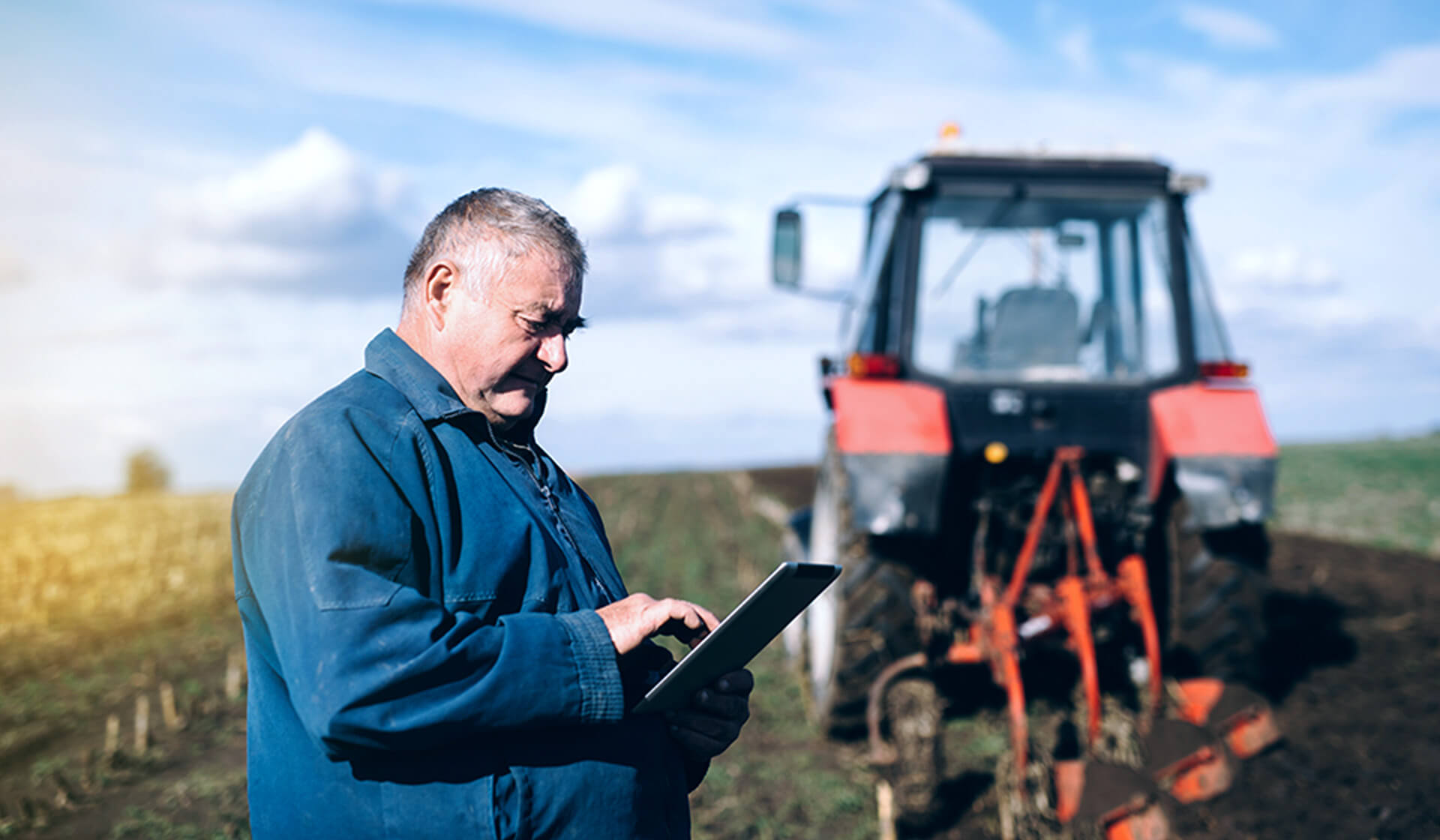 Farmer using a tablet on field with red tractor in the background