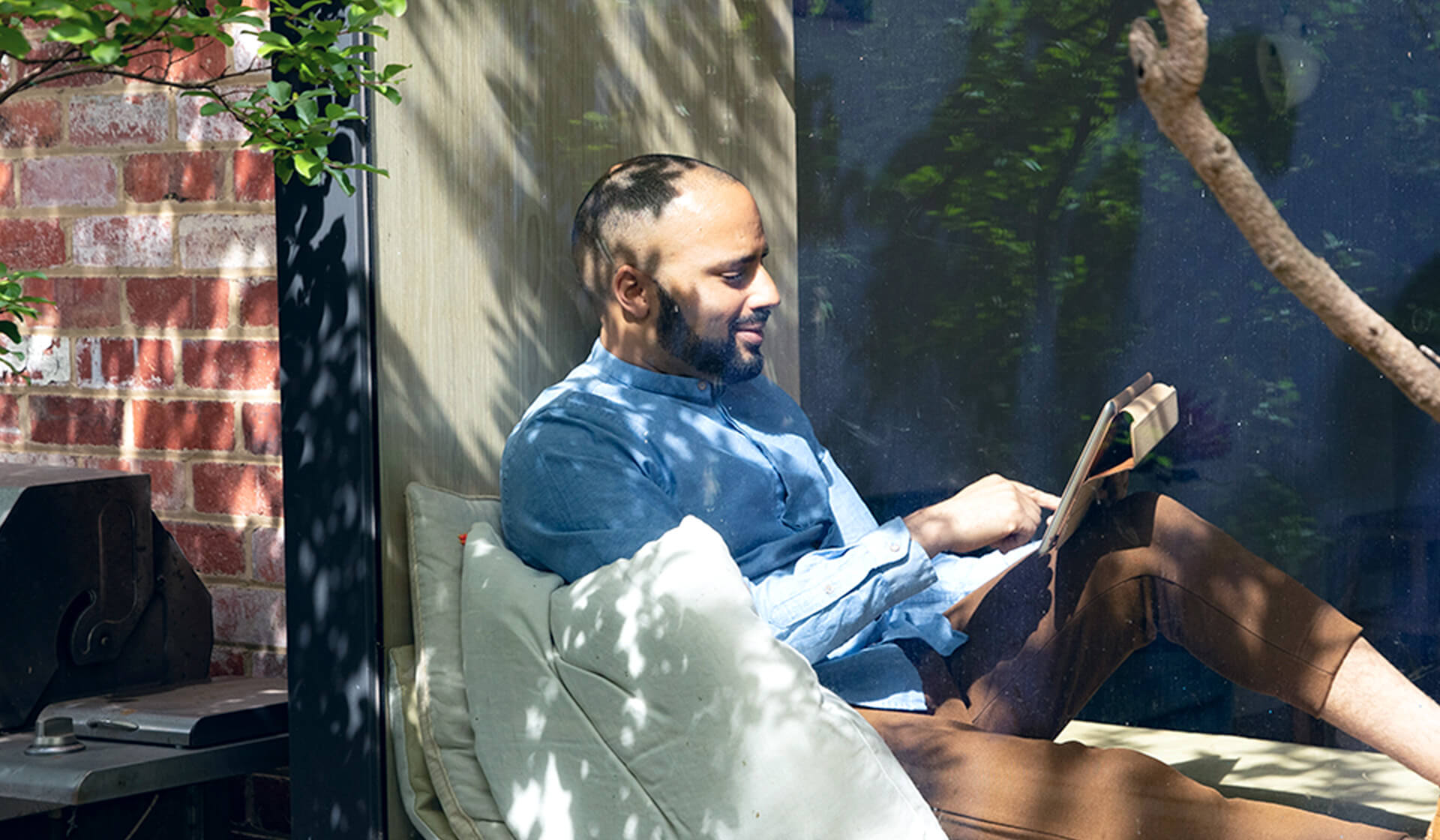 Smiling man reading on tablet at cosy window seat