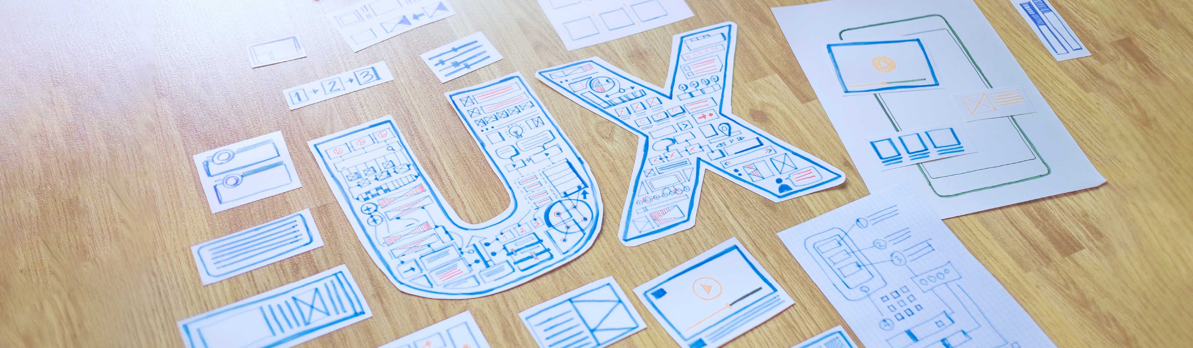 Multiple pieces of paper with wireframes and a cut out of the letters 'UX'