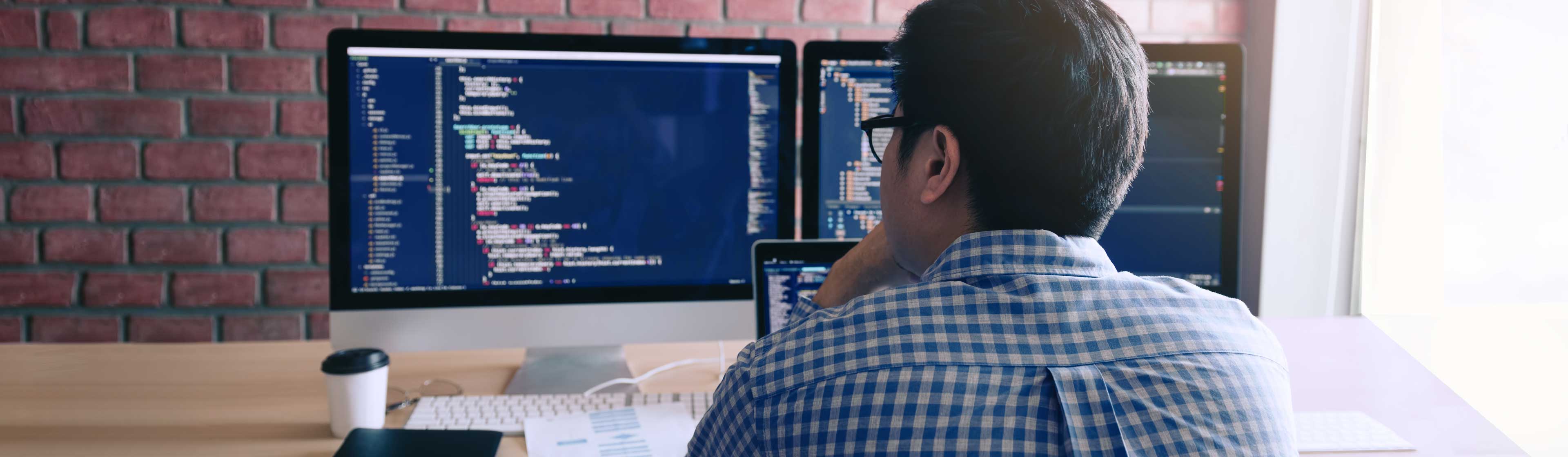 A software engineer wearing glasses coding at his computer