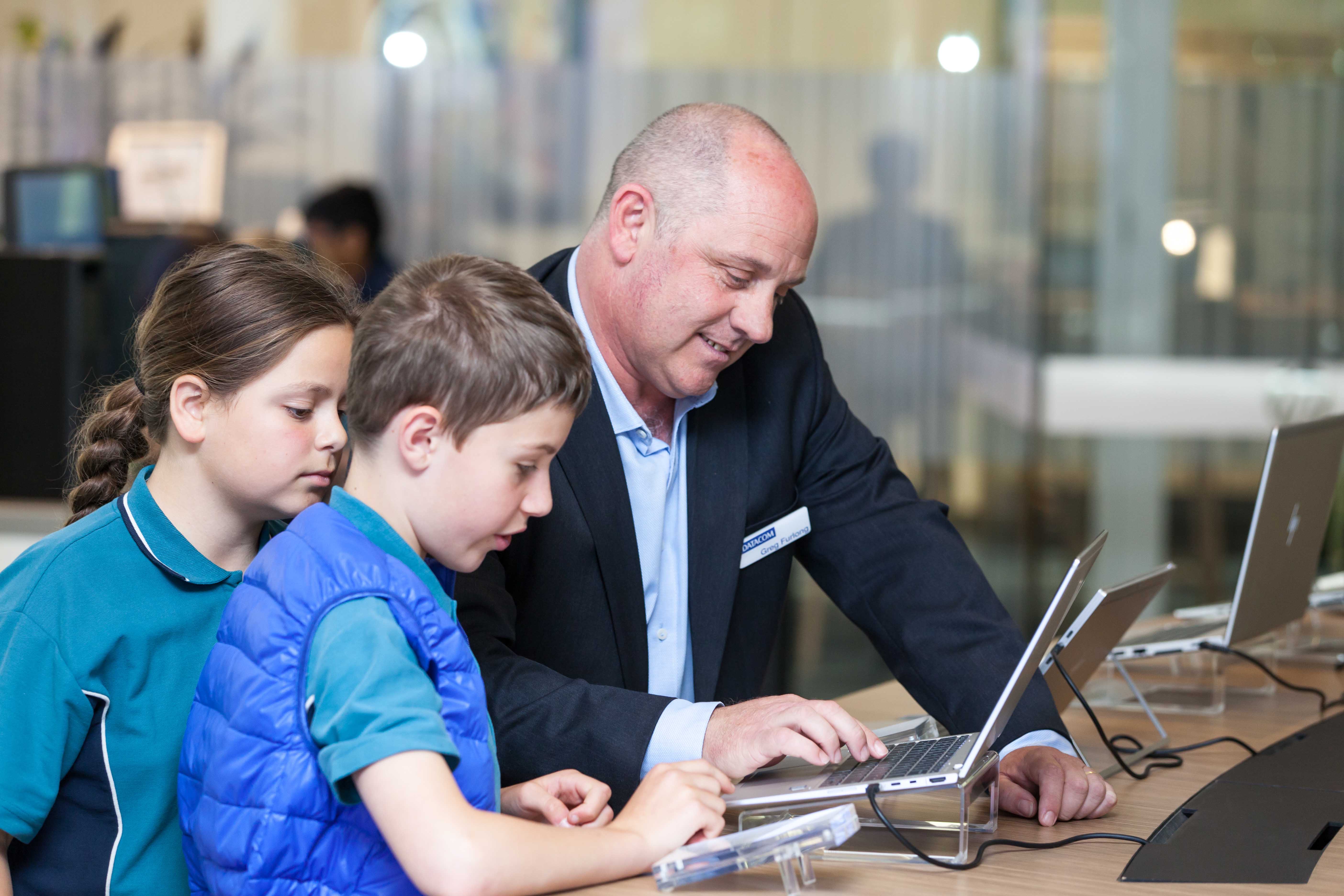 Adult man in a suit helping young students while using a laptop