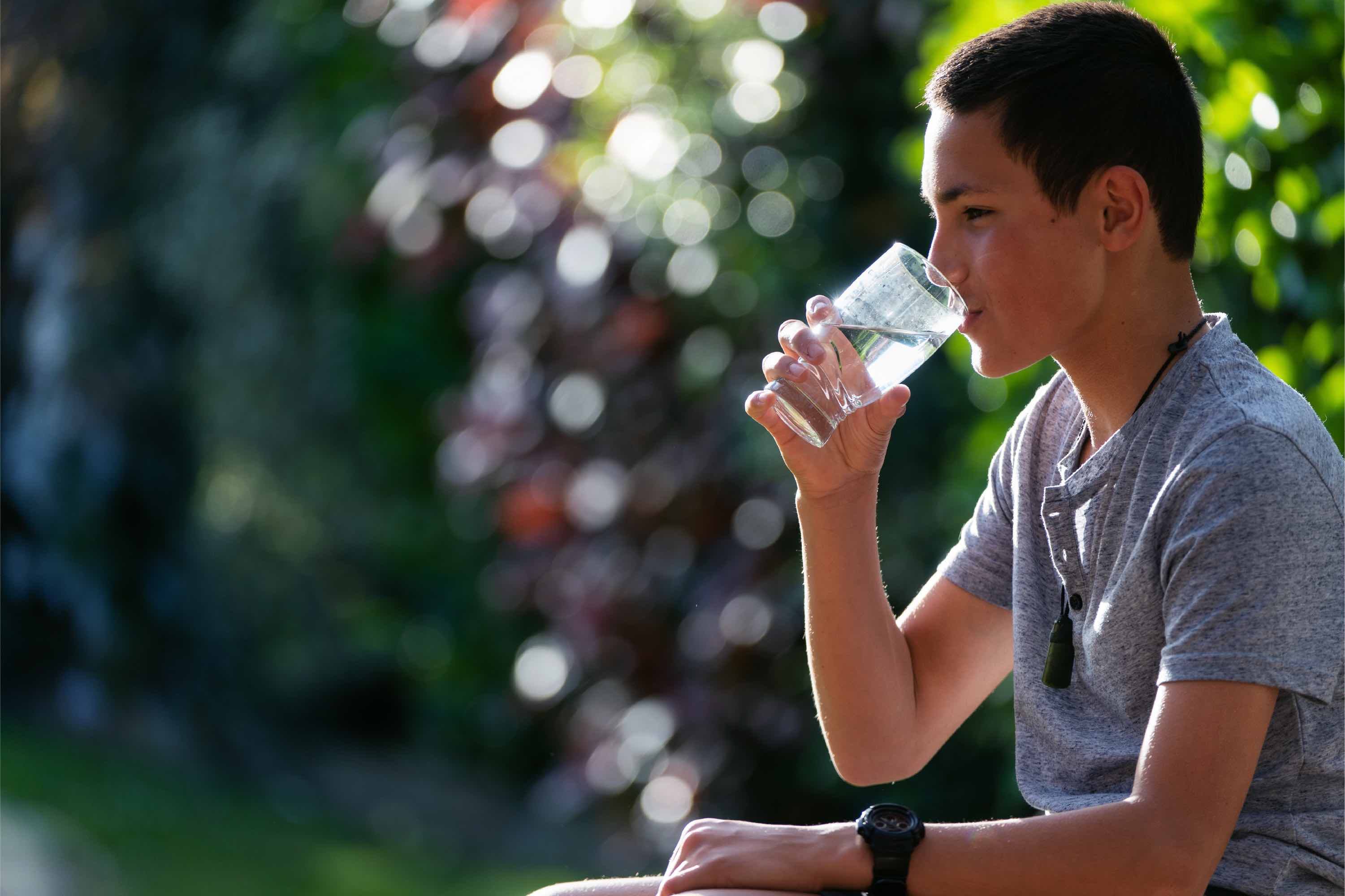 A boy sitting outside drinking from a glass of water