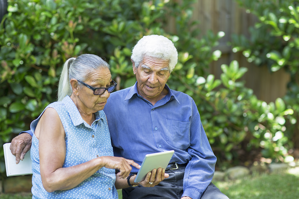 An older couple on a bench looking at a tablet 