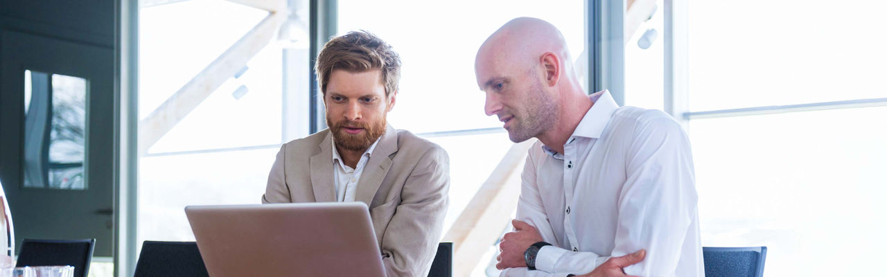 Two businessmen sharing a laptop in a conference room