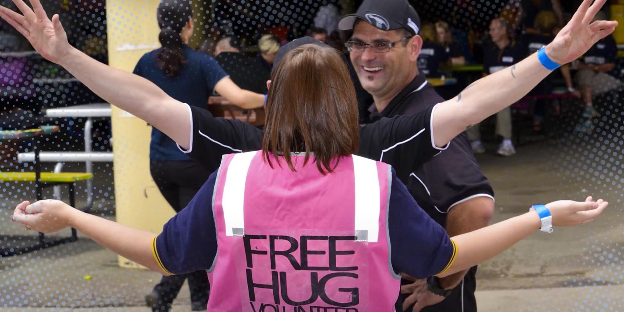 A man and a woman wearing a pink vest that says "Free hugs" 